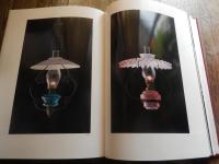 洋燈　深沢幸雄  [限定版]
藤川清撮影 ; 加藤孝次,由水常雄著
    出版社 冬樹社
    刊行年 昭和52年
    ページ数 129頁
    サイズ 21×30×3㎝ 
灯火用ガラス、とりわけランプの油壷とホヤの製造は明治のガラス工業をささえる主要分野であった。石油ランプは明治前期に急速に普及し生活の必需品となっていった。　　　　　　　　　　　　　　　　　中でも座敷ランプは、行灯や燭台のスタイルを取り入れ和洋折衷の魅力に富んでいる。また材質も鋳鉄製、朱塗り、安価なブリキ製など多様である。舶来品に匹敵するランプの制作は、明治中期以降で畳や障子に似合う日本的たおやかさを身につけた作例が生まれた。　　　　　　　　　　　　　　　　座敷ランプは、渋みとガラスの優雅さが不思議な調和をたもつ小世界を作り出す和ガラスの代表といえます。笠や油壷にガラスの加飾の粋が凝らされた卓上に置くランプ卓上に置く石油ランプ（灯油ランプ）を総称して「台ランプ」と呼びます。その中でも平芯で笠をかけない四つ爪で丸ホヤを支えたランプを「置きランブ」とし二分四つ手・五分四つ手とも呼び、巻芯のアルガン燈で円筒形の竹ホヤを冠せて笠のかかったものを「台ランプ」と区分します。笠や油壷にガラス加飾の粋が凝らされた華麗な作例が多い。座敷生活が一般的だった明治期には、紫檀や花凛、それを模した材質のランプ台が用意されることもあった。　豆ランプ。小型のランプは、仏壇、神棚、台所、風呂場、便所などに運ばれて手元を照らす明かりにされました。豆ランプ、手ランプ、吊りランプは巻き芯を用いる。大正４年の佐々木硝子店のカタログには同様の豆ランプは「豆押台」と掲載されている。　　　　　　　　
