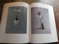 洋燈　深沢幸雄  [限定版]
藤川清撮影 ; 加藤孝次,由水常雄著
    出版社 冬樹社
    刊行年 昭和52年
    ページ数 129頁
    サイズ 21×30×3㎝ 
灯火用ガラス、とりわけランプの油壷とホヤの製造は明治のガラス工業をささえる主要分野であった。石油ランプは明治前期に急速に普及し生活の必需品となっていった。　　　　　　　　　　　　　　　　　中でも座敷ランプは、行灯や燭台のスタイルを取り入れ和洋折衷の魅力に富んでいる。また材質も鋳鉄製、朱塗り、安価なブリキ製など多様である。舶来品に匹敵するランプの制作は、明治中期以降で畳や障子に似合う日本的たおやかさを身につけた作例が生まれた。　　　　　　　　　　　　　　　　座敷ランプは、渋みとガラスの優雅さが不思議な調和をたもつ小世界を作り出す和ガラスの代表といえます。笠や油壷にガラスの加飾の粋が凝らされた卓上に置くランプ卓上に置く石油ランプ（灯油ランプ）を総称して「台ランプ」と呼びます。その中でも平芯で笠をかけない四つ爪で丸ホヤを支えたランプを「置きランブ」とし二分四つ手・五分四つ手とも呼び、巻芯のアルガン燈で円筒形の竹ホヤを冠せて笠のかかったものを「台ランプ」と区分します。笠や油壷にガラス加飾の粋が凝らされた華麗な作例が多い。座敷生活が一般的だった明治期には、紫檀や花凛、それを模した材質のランプ台が用意されることもあった。　豆ランプ。小型のランプは、仏壇、神棚、台所、風呂場、便所などに運ばれて手元を照らす明かりにされました。豆ランプ、手ランプ、吊りランプは巻き芯を用いる。大正４年の佐々木硝子店のカタログには同様の豆ランプは「豆押台」と掲載されている。　　　　　　　　
